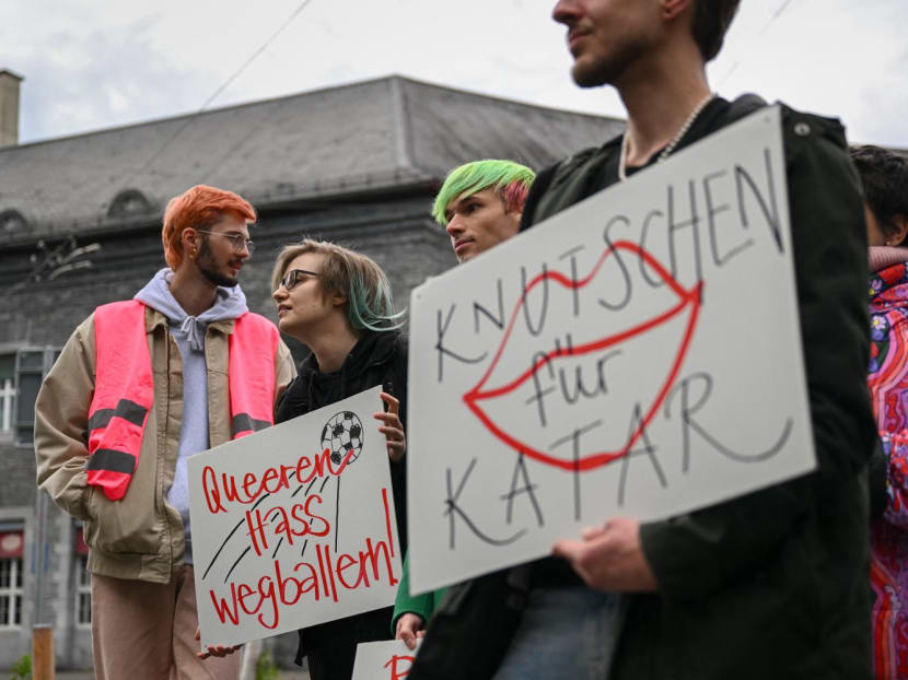 Activists hold boards reading in German "shooting at queer hate" and "Smooching for Qatar" during a symbolic action by LGBT+ associations in front of the FIFA museum in Zurich on Nov 8, 2022.