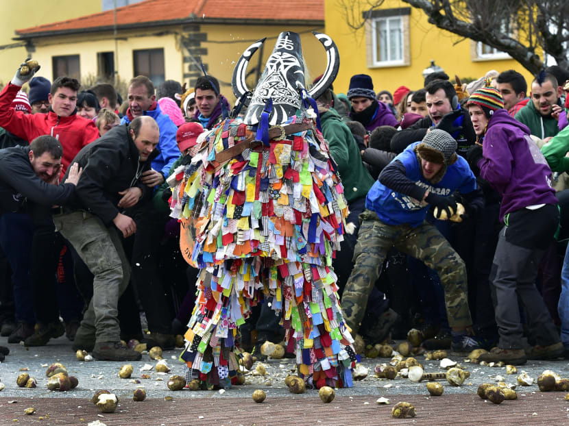 People throw turnips at a man representing the Jarrampla, beating his drum and sporting a costume covered in multicoloured ribbons and his face hidden behind a conical mask with a huge nose, horns and a horse's mane. Photo: AFP