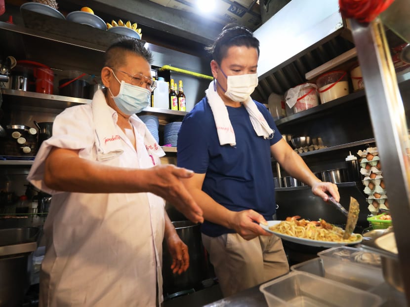 Mr Kang Kaiming (left) showing his mentee Louis Wong how to serve Hokkien prawn noodles at Geylang East Market and Food Centre. Mr Kang Kaiming (left) showing his mentee Louis Wong how to serve Hokkien prawn noodles at Geylang East Market and Food Centre.