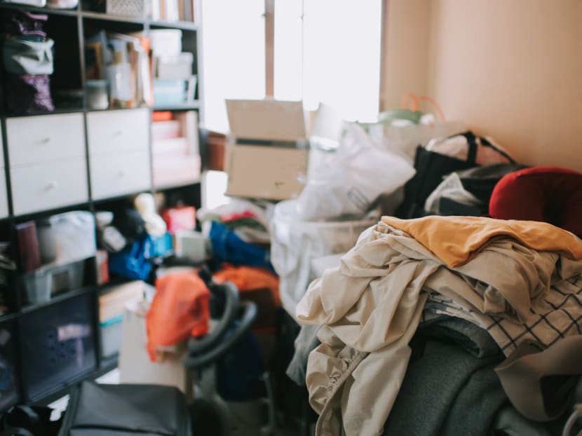 Clothes, bags, boxes and things piled high in a room, with shelving space also packed full of items.