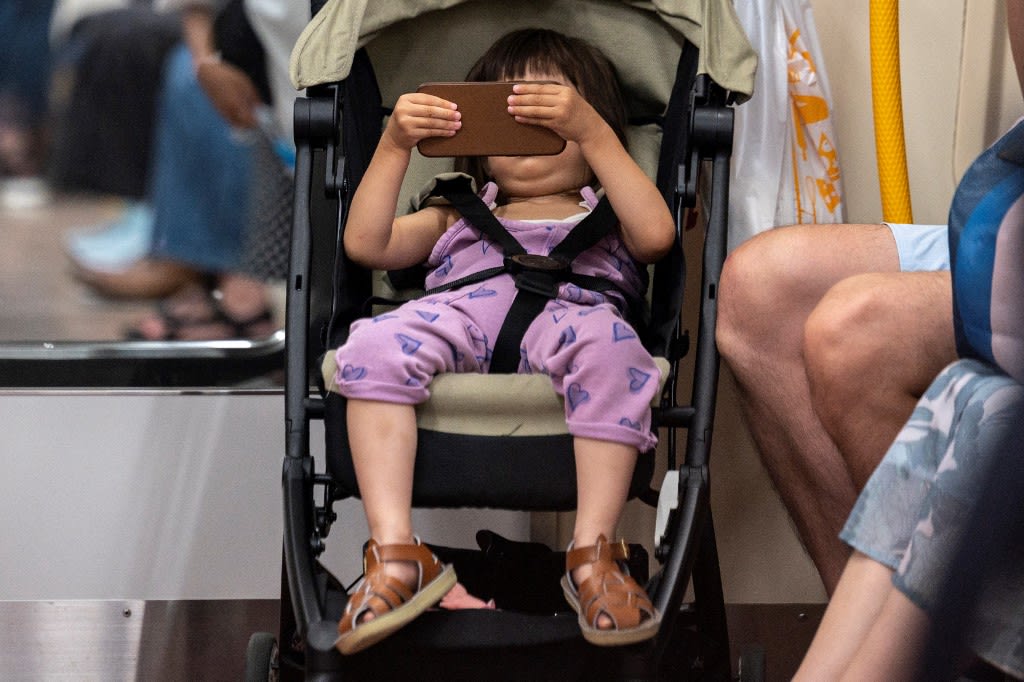 A toddler looks at a smartphone in a train in Tokyo on July 24, 2021.