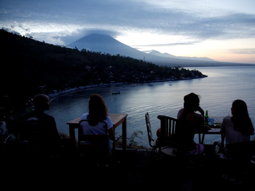 Tourists have a drink while watching the sunset behind Mount Agung, a volcano on the highest alert level, in Amed on the resort island of Bali, Indonesia. Photo: Reuters