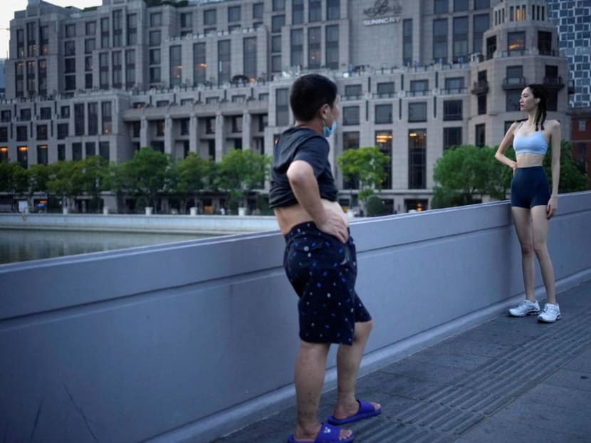 A woman poses for a photo on a bridge near the Bund amid a heatwave warning, as Shanghai switches off lights along a popular waterfront to conserve energy in Shanghai, China