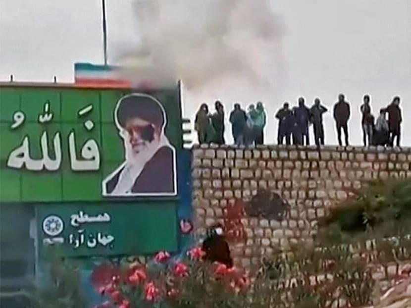 This image grab from a UGC video posted on Nov 3, 2022, reportedly shows protesters throwing a small explosive device at a banner depicting the Islamic Republic's Supreme Leader Ayatollah Ali Khamenei, as a large crowd enters the district of Fuladshahr near the central city of Isfahan.

