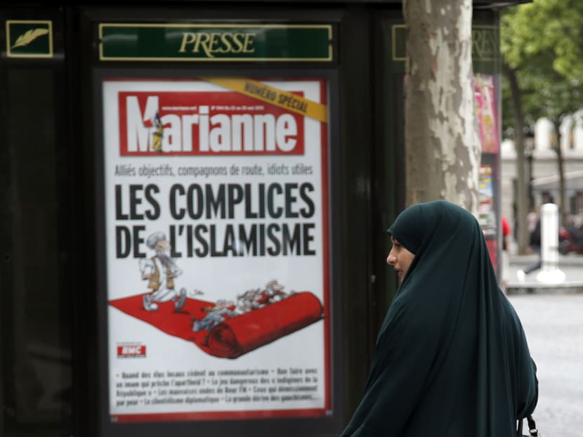 In this Thursday, May 21, 2015 photo a Muslim woman walks by a poster for French magazine Marianne reading "Radical Islam Accomplice", on the Champs Elysees in Paris. Photo: AP