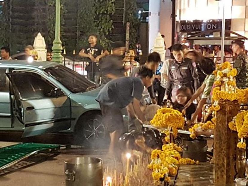 Police help tend to injured people after a car struck the fence and stopped inside the Erawan Shrine compound on Friday night. Photo: @JS100 and @Wita007/Twitter
