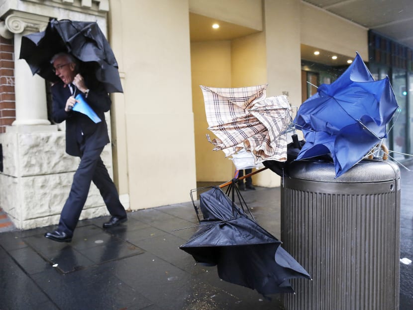 A man takes shelter next to discarded broken umbrellas in a litter bin during heavy rain in the Sydney central business district, on Tuesday April 21, 2015. Photo: AP