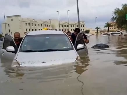 In this video grab from AFPTV, people push a stranded car along a flooded street in Dubai on April 16, 2024.