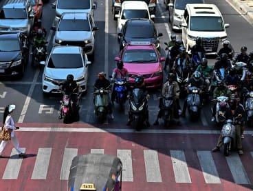 Motorcyclists wait under the shade as a woman crosses a traffic intersection in Bangkok on April 25, 2024. 