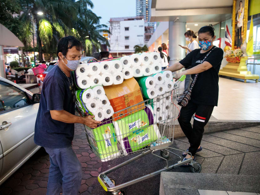 People wearing face masks push a shopping cart full of toilet paper and kitchen rolls at a supermarket in Bangkok on March 16, 2020.