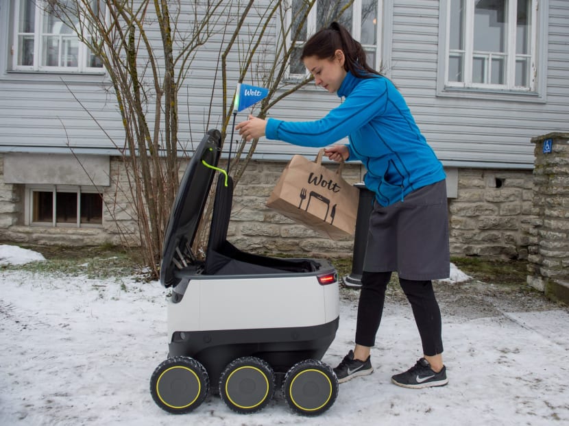 A woman takes delivery of food from a six-wheeled robot by Starship Technologies from restaurant in Tallinn, Estonia on February 16, 2017. The knee-high, black-and-white robot carefully avoids pedestrians, stops obediently at the red traffic light of a large road junction. Photo: AFP