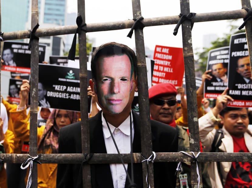 A man wearing a mask depicting Australian Prime Minister Tony Abbott stands behind a bamboo fence during a student protest against Abbott in front of the Australian embassy in Jakarta on February 25, 2015. Photo: Reuters