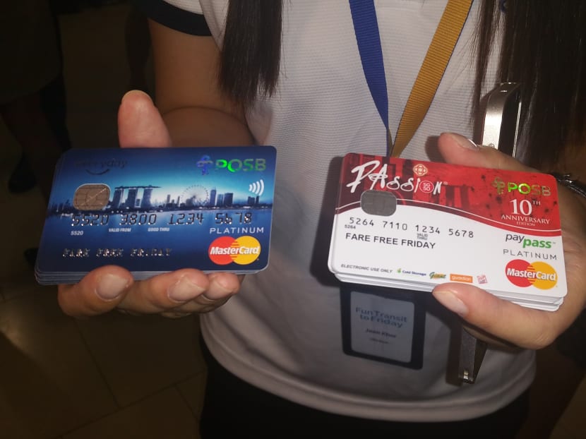A POSB employee holding up POSB Everyday Credit Cards and PAssion POSB Debit Cards that cardholders can use to enjoy unlimited free MRT, LRT and bus rides every Friday till the end of this year. Photo: Amanda Lee