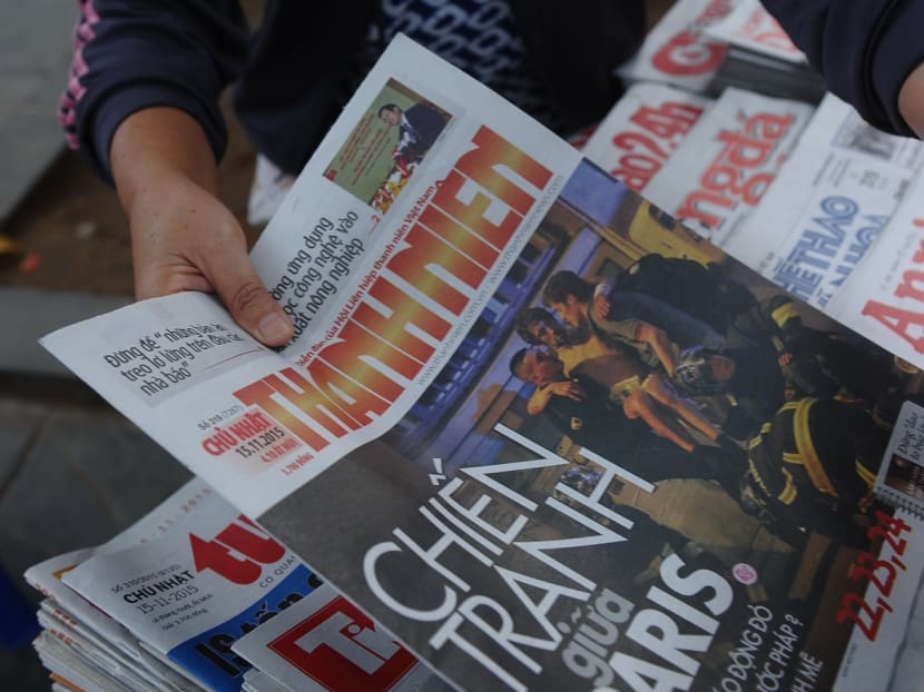 A Vietnamese vendor picks up newspapers with photos and headlines about the Paris terrorist attacks on November 15, 2015. Photo: AFP