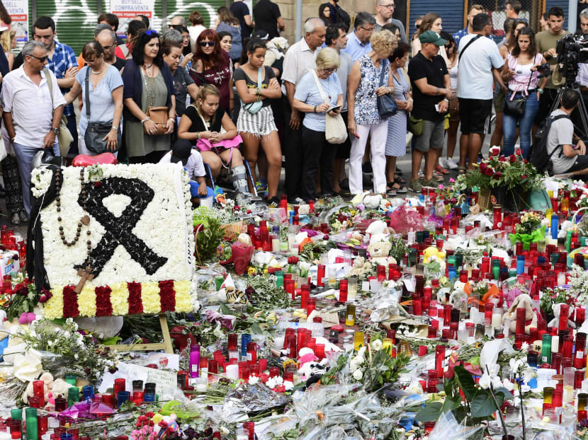 People stand next to flowers, candles and other items set up on the Las Ramblas boulevard in Barcelona as they pay tribute to the victims of the Barcelona attack Photo: AFP