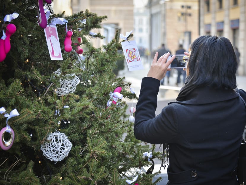 A woman takes a picture of the ‘Tree of Pleasure’ in downtown Milan before its racy red sex toys were removed from its branches. Photo: AP
