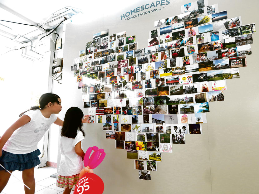 Two girls put a photograph on the photo wall mosaic at the SG Heart Map HomeScapes Photography Exhibition, which invites Singaporeans to share what defines Singapore as home for them, by attaching photographs contributed by fellow Singaporeans to the SG Heart Map (新心相印). Photo: Ooi Boon Keong/TODAY