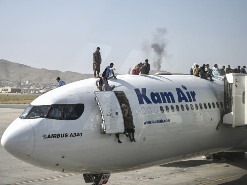 Afghan people climb atop a plane as they wait at the Kabul airport in Kabul on Aug 16, 2021, after a stunningly swift end to Afghanistan's 20-year war, as thousands of people mobbed the city's airport trying to flee the group's feared hardline brand of Islamist rule.