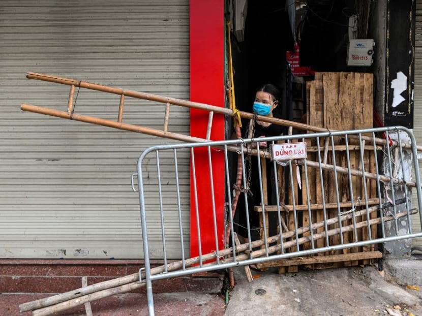 This photograph taken on Aug 30, 2021 shows a woman looking out from behind an improvised barricade made of wooden planks and a ladder to restrict residents' movements in Hanoi, as part of the authorities' plan to stop the spread of the Covid-19 coronavirus.