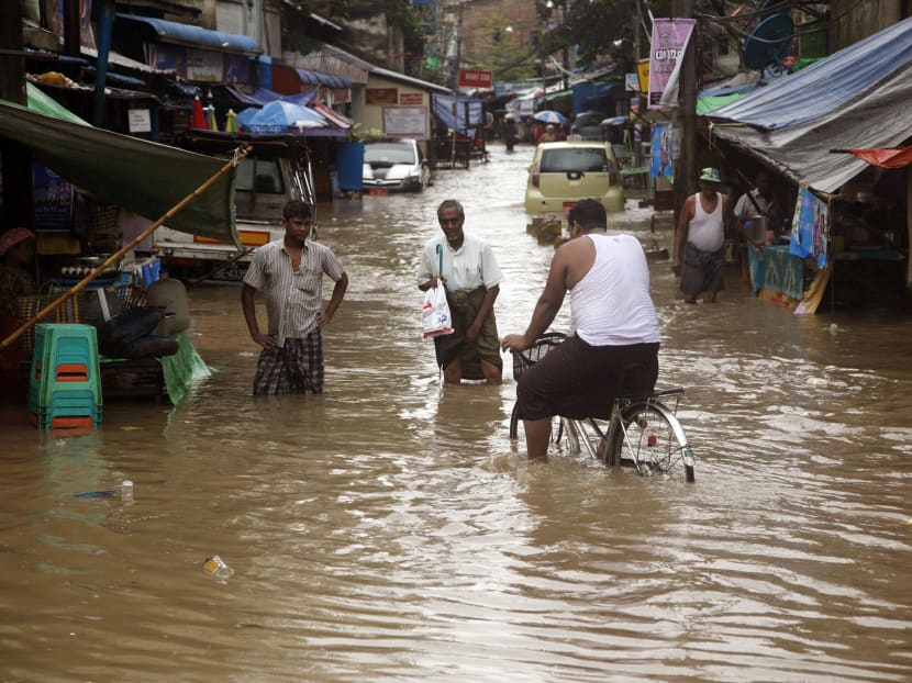 A man rides bicycle as pedestrians walk on a flooded road caused by heavy rain Tuesday, July 28, 2015, Yangon, Myanmar. Photo: AP