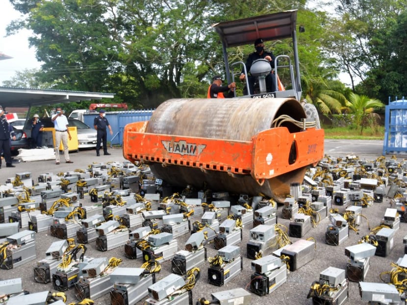 This handout photo taken on July 16, 2021 shows police at the Miri district police headquarters using a steamroller to crush bitcoin-mining machines, in the Malaysian Borneo city of Miri.