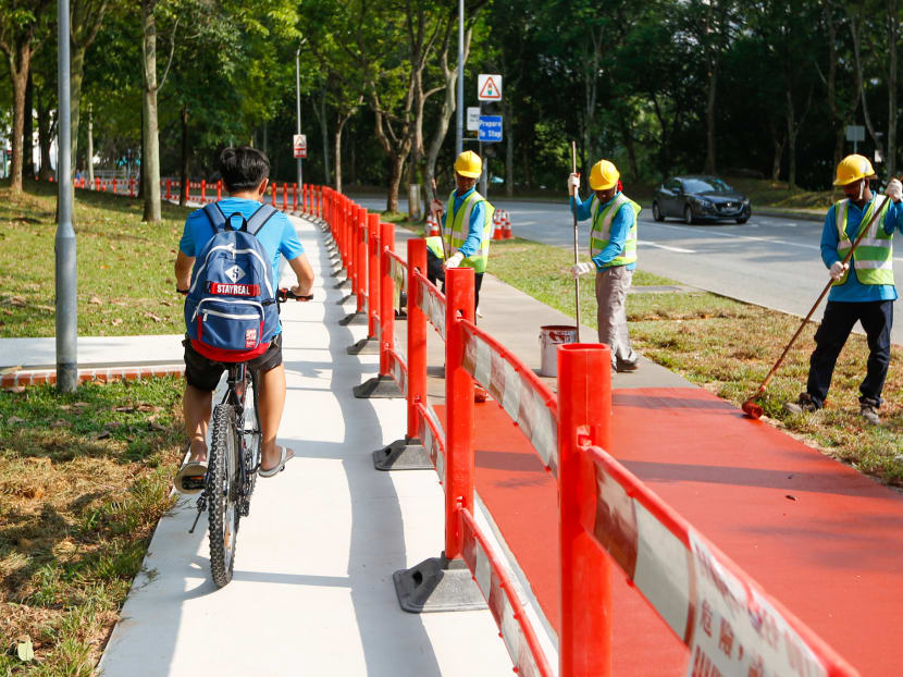 A cyclist rides by as the shared path along Saujana Road, in the Bukit Panjang area, is painted by workers on March 11, 2020.