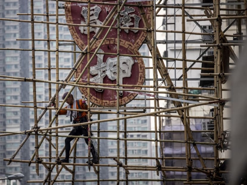 This picture taken in Hong Kong on March 9, 2023 shows a scaffolder constructing bamboo scaffolding around a neon sign. 