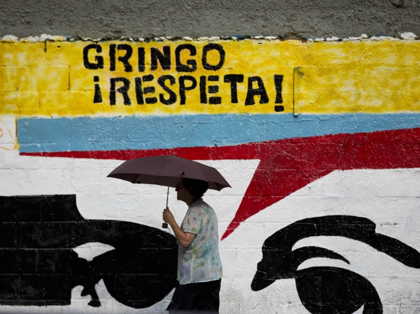 A woman using an umbrella during a drizzle walks by a mural representing the eyes of Venezuela's independence hero Simon Bolivar that reads in Spanish "Gringo, respect!" in Caracas, Venezuela on March 2 this year. Photo: AP