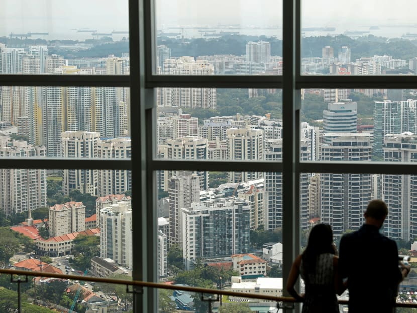 People stand in front of a view of public housing and private residential condominiums in Singapore. 