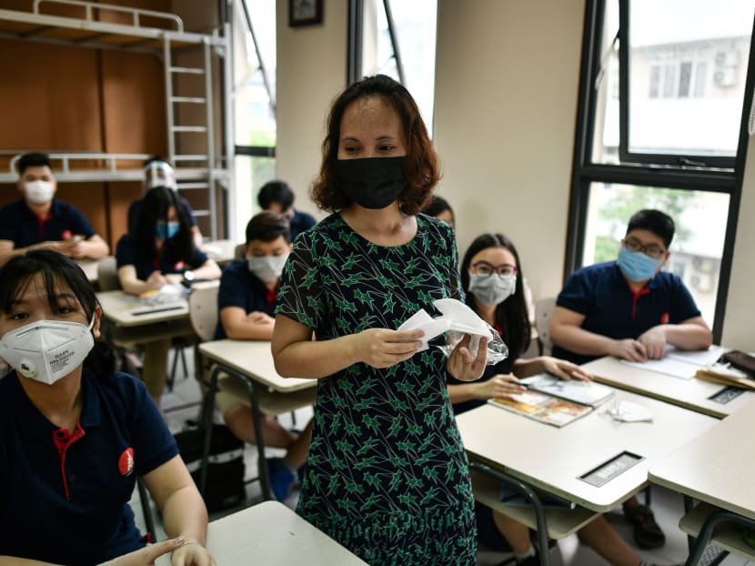 A teacher distributes face masks to students inside a classroom at the Marie Curie school in Hanoi, Vietnam on May 4, 2020.
