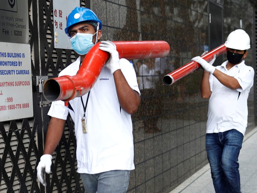 Construction workers wearing masks in precaution of the coronavirus outbreak carry pipes as they pass a building in the Central Business District in Singapore on February 18, 2020.