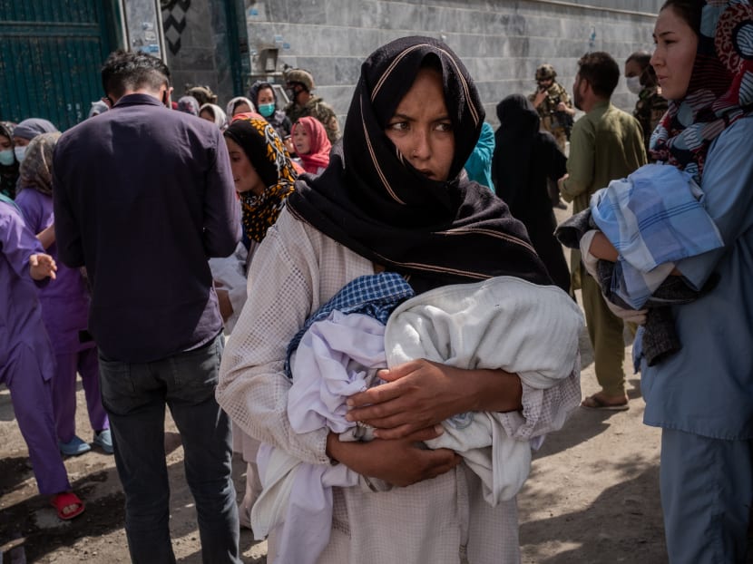 A woman carrying a baby stands among a crowd near a hospital in Kabul, Afghanistan, that was attacked on May 12, 2020.