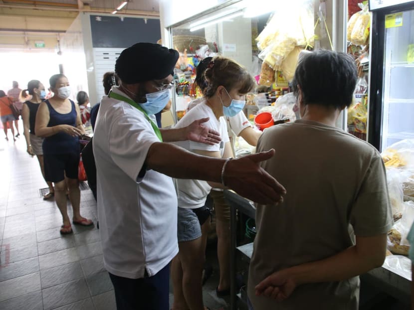 A National Environment Agency (NEA) officer reminding patrons to keep a safe distance from each other at a stall during an enforcement operation at Chong Boon Market on April 10, 2020.