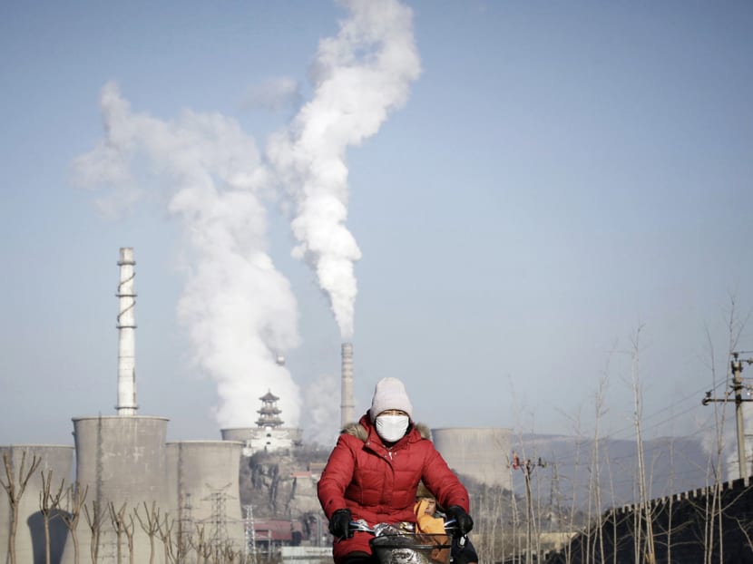 A woman wearing a mask riding past smoking chimneys and cooling towers of a steel plant in Beijing. China, the world’s biggest polluter, has refused to accept international monitoring of its emissions and says it will provide data to outside observers. Photo: Reuters