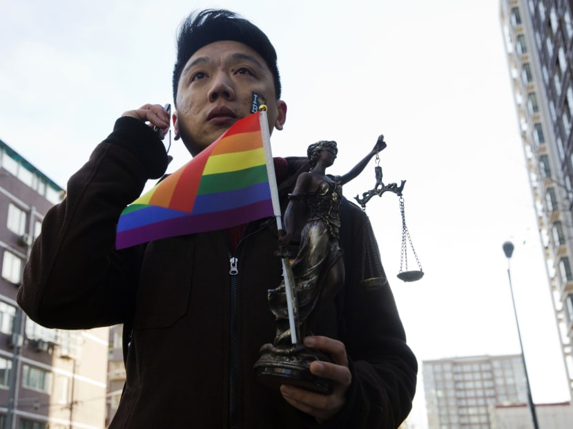 Yang Teng holds up a statue depicting a goddess of justice and a rainbow color flag as he arrives to attend a court verdict in Beijing, China, Dec 19, 2014.  Photo: AP