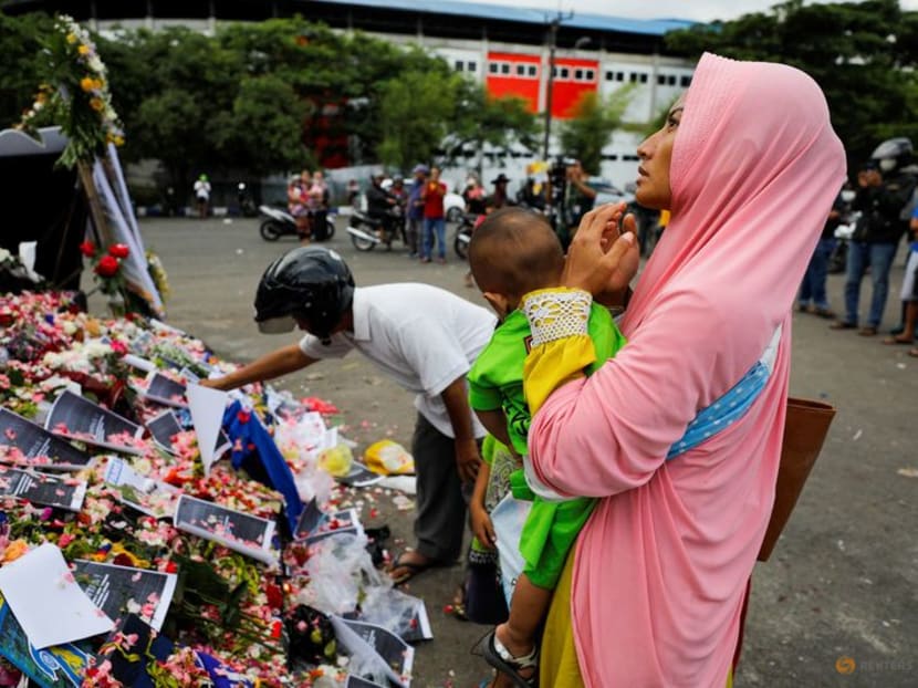 A woman carrying her child prays on a monument as she pays condolence to the victims after a riot and stampede following soccer match between Arema vs Persebaya, outside the Kanjuruhan stadium in Malang, East Java province, Indonesia, October 3, 2022. REUTERS/Willy Kurniawan
