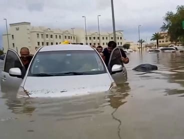 In this video grab from AFPTV, people push a stranded car along a flooded street in Dubai on April 16, 2024.
