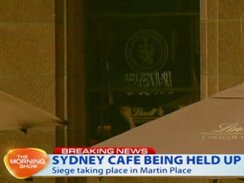 This image taken from video shows people holding up what appeared to be a black flag with white Arabic writing on it, inside a cafe in Sydney, Australia Dec 15, 2014. Photo: AP/Channel 7