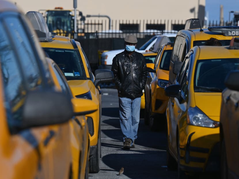 A yellow cab taxi driver walks between cars as he waits in line at a taxi hold at LaGuardia Airport in New York City on February 4, 2021. They were omnipresent on the streets of New York day and night, as emblematic of the Big Apple as the Empire State Building or Yankees caps. But the pandemic has made yellow taxis scarce and facing an uncertain future.
