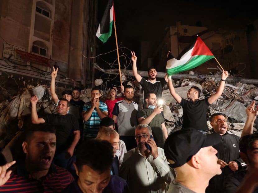 A man waves the Palestinian flag and others flash the V-sign for victory as they celebrate, in front of a destroyed building, the ceasefire brokered by Egypt between Israel and the two main Palestinian armed groups in Gaza on May 20, 2021.