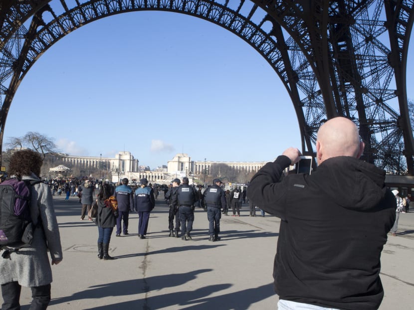 A tourist takes photographs, right, as French police patrol under the Eiffel Tower in Paris, Saturday, Jan. 17, 2015. Since last week’s terrorist attacks that killed 17 people in Paris, the swarms of sightseers have thinned below Paris’ most visited monument, the Eiffel Tower. Photo: AP