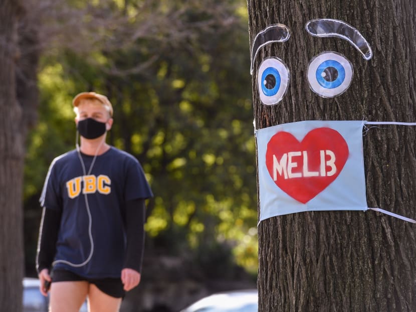 A man walks past a large face mask pinned to a tree in Melbourne on August 3, 2020 after the state announced new restrictions as the city battles fresh outbreaks of the Covid-19 coronavirus.