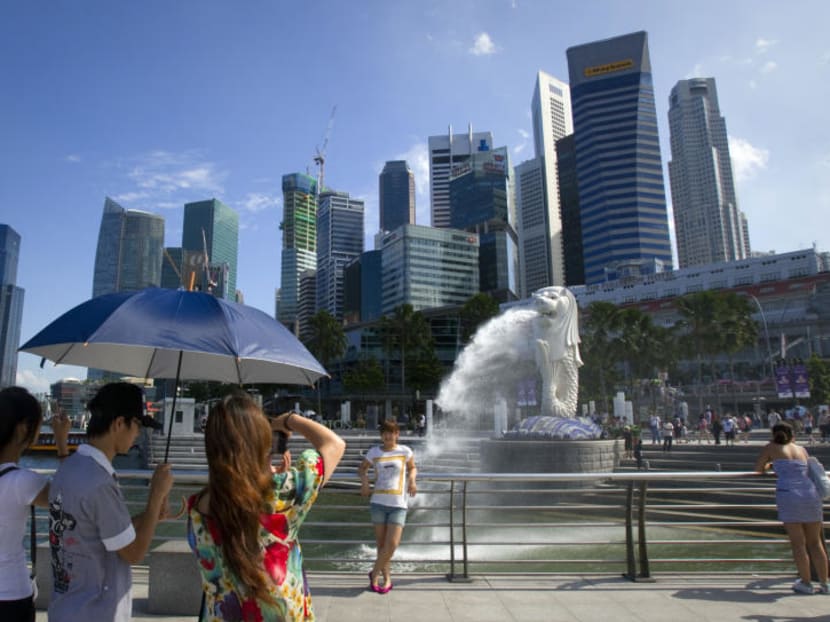A tourist poses for a photo in front of the Merlion, a mascot of Singapore, and the financial district skyline in Singapore. Photo: Reuters