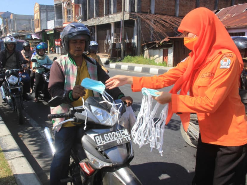 An Aceh Barat goverment official gives mask to motorcyclists as haze from peatland fires hits the city in Meulaboh, Indonesia. Photo: Reuters