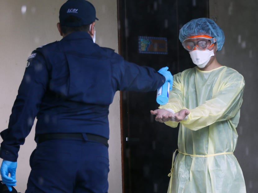 An officer from the Singapore Civil Defence Force at a Government quarantine facility disinfecting the hands of a medical worker.