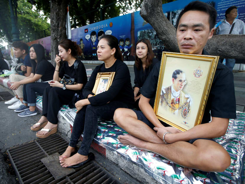 Thais sitting by the roadside in Bangkok as they await the funeral procession of King Bhumibol. Photo: Reuters