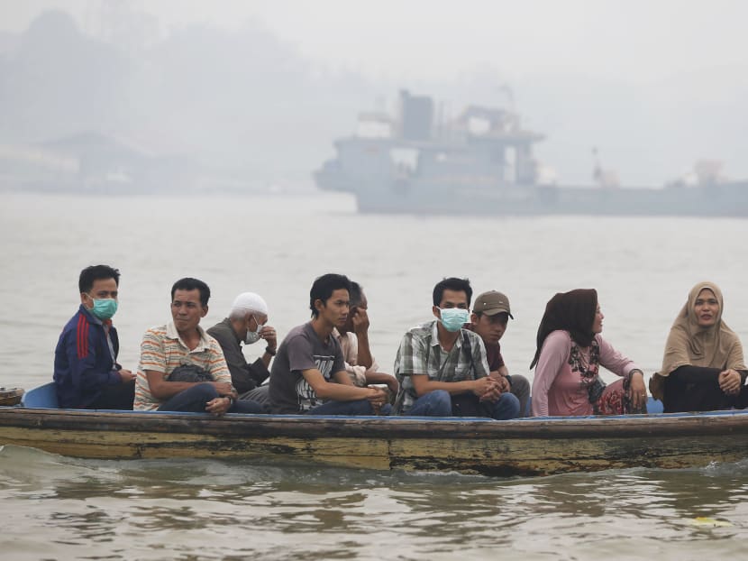 People sit on a wooden boat as they cross the haze shrouded Batanghari River in Jambi, Indonesia Sumatra island, Sept 14, 2015. Photo: Reuters