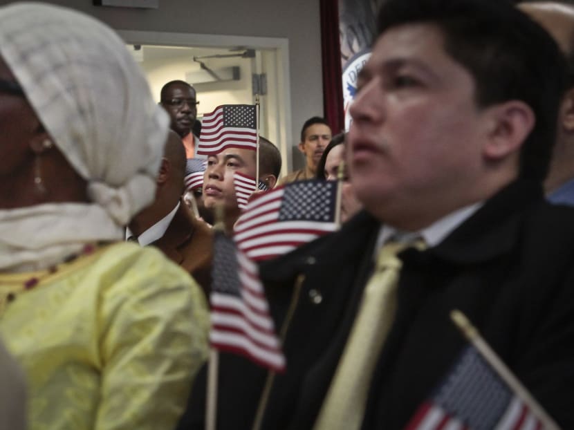 In this Dec 18, 2013 file photo, immigrants hold miniature US flags as they listen to a video broadcast from President Barack Obama during a naturalisation ceremony. Photo: AP