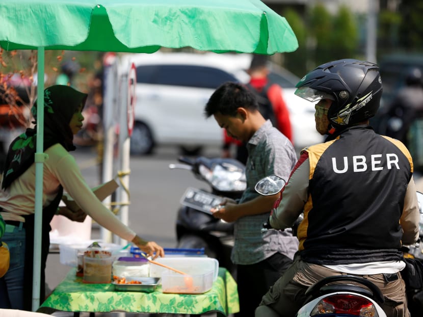 An Uber motorcycle taxi driver stops at a food stall in Jakarta, Indonesia. Uber is said to be relooking its Asia businesses. Photo: Reuters