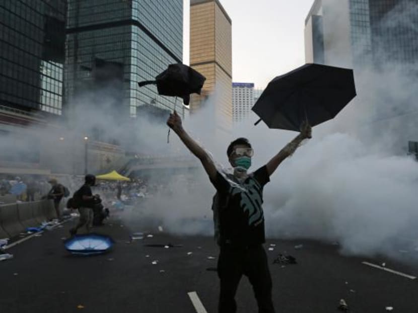 A protester raises his umbrellas in front of tear gas which was fired by riot police to disperse protesters blocking the main street to the financial Central district outside the government headquarters in Hong Kong, Sept 28, 2014. Photo: Reuters